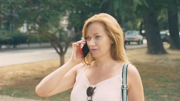 Mujer joven y feliz hablando por teléfono, caminando por el paseo marítimo en un caluroso día soleado de verano. 4k, cámara lenta — Vídeos de Stock