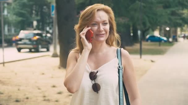 Mujer joven y feliz hablando por teléfono, caminando por el paseo marítimo en un caluroso día soleado de verano. 4k, cámara lenta — Vídeos de Stock