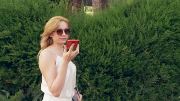 Šťastná mladá žena mluví o telefonu, procházky po nábřeží na horký slunečný letní den. 4k, pomalý pohyb — Stock video