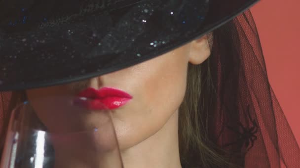 Bela jovem mulher sexy em um traje de bruxa preta e chapéu, com um copo de vinho e uma vassoura olha para a câmera e sorri. espaço de cópia. 4k, câmera lenta, super close-up — Vídeo de Stock