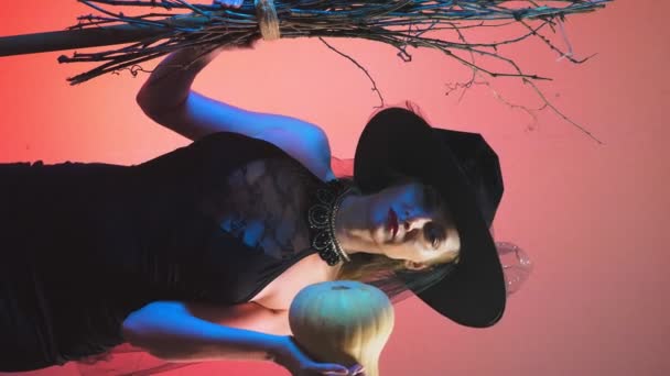 Красивая молодая сексуальная женщина в черном костюме ведьмы и шляпе, с тыквой в руках. скопировать пространство. 4k, slow motion — стоковое видео