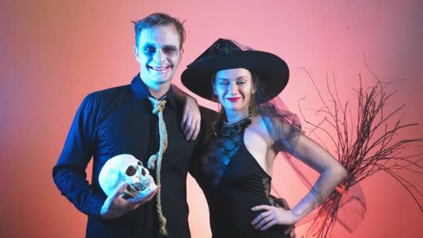 Una hermosa pareja, un hombre y una mujer con disfraces de brujas y zombis para Halloween, 4k, cámara lenta, sostienen el cráneo en sus manos. La felicitación por la fiesta , — Vídeo de stock