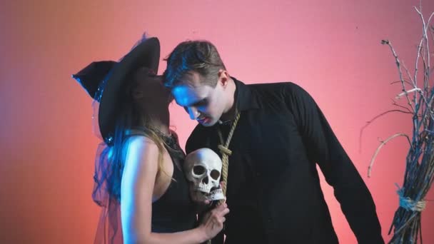 Piękna para, mężczyzna i kobieta w czarownica i zombie kostiumy na Halloween, 4k, zwolnionym tempie, czaszka trzymać w rękach. Gratulacje na wakacje, — Wideo stockowe