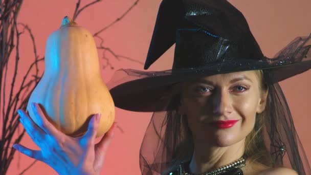 Bella giovane donna sexy in costume da strega nera e cappello, con una zucca in mano. copiare spazio. 4k, rallentatore — Video Stock