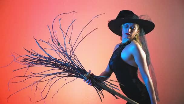Güzel genç seksi kadın kara cadı kostüm ve bir süpürge ile şapka içine belgili tanımlık fotoğraf makinesi ve gülümseyerek bakar. kopya alanı. 4k, ağır çekim — Stok video