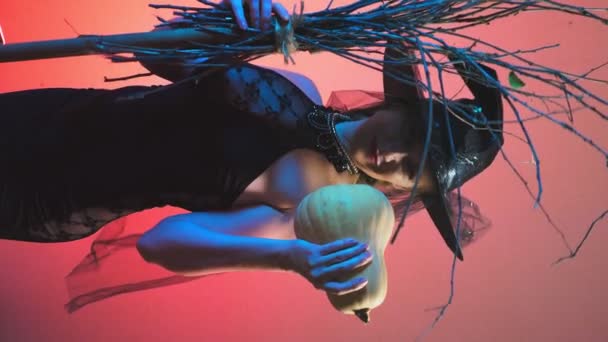 Hermosa joven sexy mujer en un traje de bruja negro y sombrero, con una calabaza en sus manos. espacio de copia. 4k, cámara lenta — Vídeo de stock