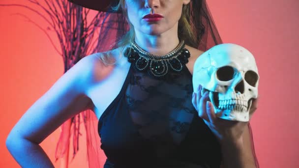 Beautiful young sexy woman in a black witch costume and hat, with a broom and a skull in her hands. copy space. 4k, slow motion — Stock Video