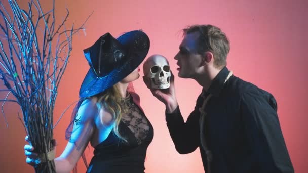 Un beau couple, un homme et une femme en costumes de sorcière et de zombie pour Halloween, 4k, au ralenti, tenir le crâne dans leurs mains. félicitations pour les vacances , — Video