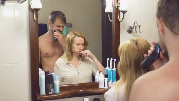 Bella coppia, uomo e donna, lavarsi insieme nel bagno di fronte allo specchio. 4k, rallentatore, una donna si lava i denti, un uomo si depila . — Video Stock