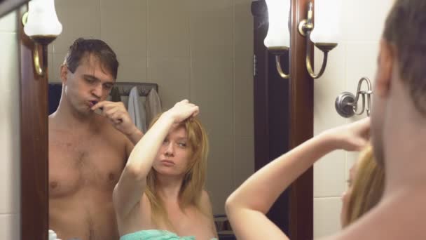 Piękna para, mężczyzna i Kobieta, myć razem w łazience przed lustrem. 4k, zwolnionym tempie, człowiek jest szczotkowanie zęby, kobieta robi Stylizacja włosów. — Wideo stockowe