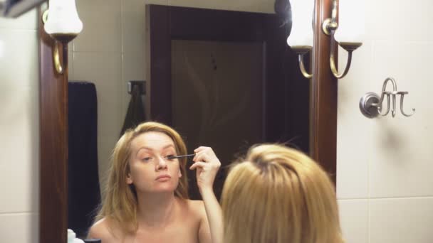4k. Медленное движение. Женщина красит ресницы перед зеркалом в ванной комнате — стоковое видео