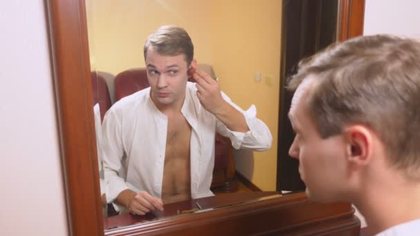 O conceito de metrosexualismo. Um homem bonito à frente de um espelho cuida do seu rosto. faz o contorno do rosto, maquiagem cotidiana. 4k, câmera lenta — Vídeo de Stock