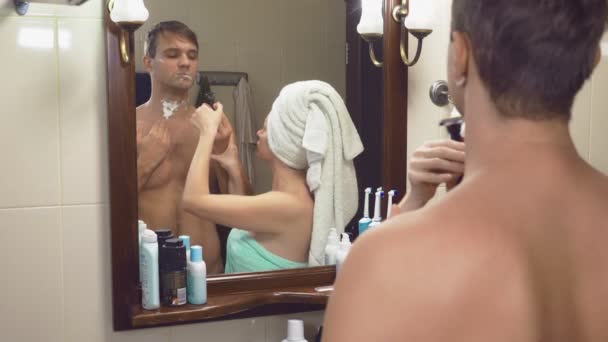 Vackert par, man och kvinna, tvätta tillsammans i badrummet framför spegeln. 4k, ultrarapid, tar kvinna rakhyveln från hennes make och startar rakning hennes armhålor — Stockvideo