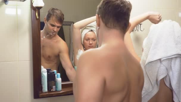 Belo casal, homem e mulher, lavar juntos no banheiro em frente ao espelho. 4k, câmera lenta, a mulher tira a navalha de seu marido e começa a raspar suas axilas — Vídeo de Stock