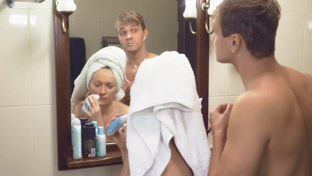 Mooi Stel, man en vrouw, wassen samen in de badkamer voor de spiegel. 4k, slow motion, de man scheert zijn gezicht met een machine tool, een vrouw maakt een epileren van het haar op haar — Stockvideo