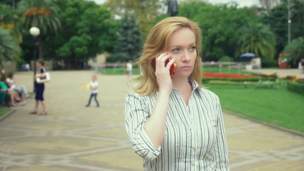 Vrouw blond is praten over de telefoon op de vlucht, ze is in een haast. buiten in de zomer. Slow-motion — Stockvideo