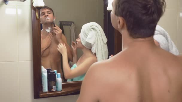 Красивая пара, мужчина и женщина, мыться вместе в ванной комнате перед зеркалом. 4К, замедленная съемка, женщина берет бритву у мужа и начинает брить подмышки — стоковое видео