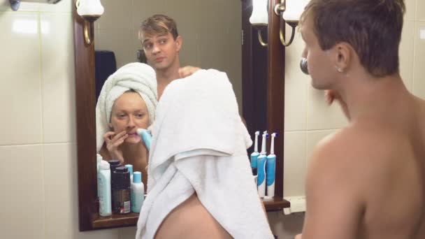Красивая пара, мужчина и женщина, мыться вместе в ванной комнате перед зеркалом. 4к, замедленная съемка, муж бреет лицо станком, женщина делает эпиляцию волос на ней — стоковое видео