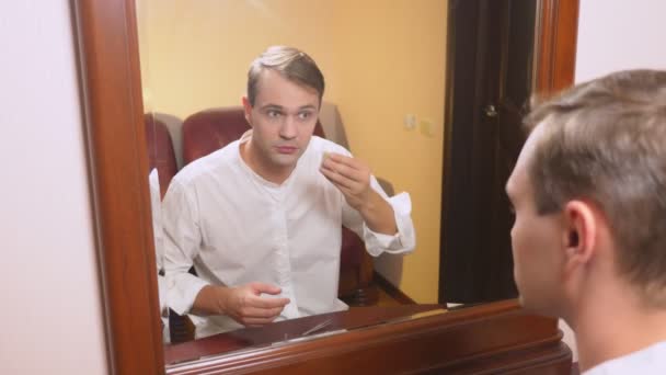 El concepto de metrosexualismo. un hombre guapo delante de un espejo cuida su cara. hace el contorno de la cara, maquillaje todos los días. 4k, cámara lenta — Vídeo de stock