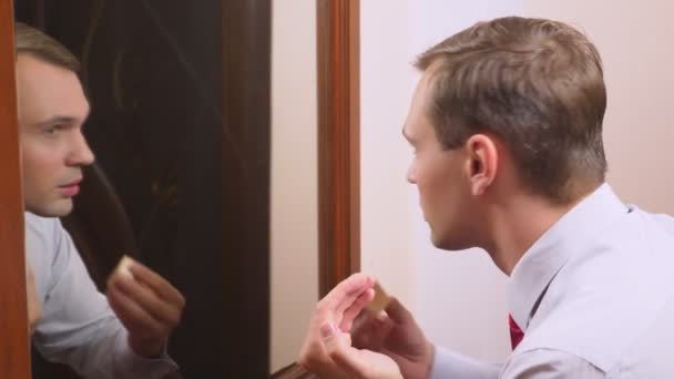 Het concept van metrosexualism. een knappe man in een spiegel zorgt voor zijn gezicht. doet de contouren van het gezicht, dagelijkse make-up. 4k, slow-motion — Stockvideo