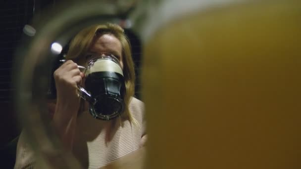 Женщина пьет тёмное свежее пиво из стакана в ночном клубе — стоковое видео