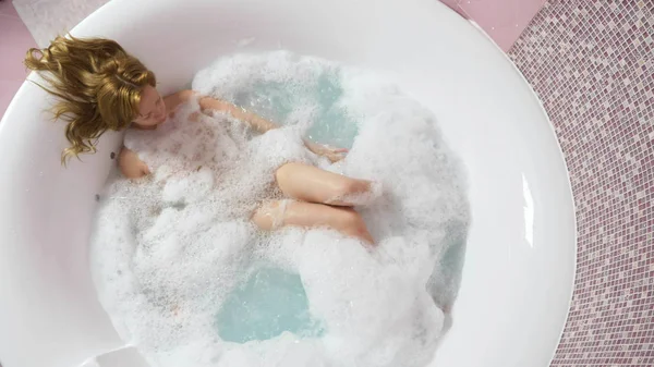 Belle jeune femme se détend dans un bain avec hydromassage, sur un fond bleu. Concept : procédures de spa, massage du corps, crème spa, relaxation, traitements de l'eau. vue d'en haut — Photo