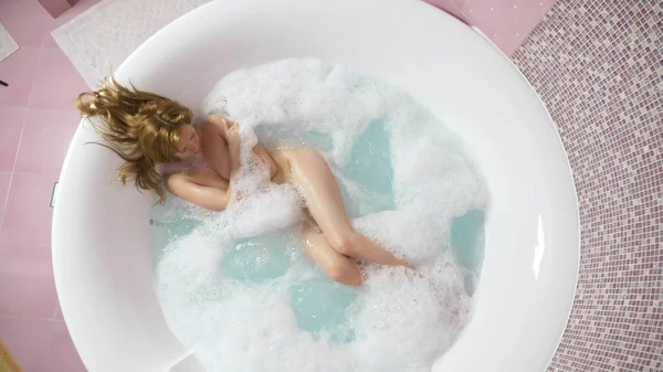 Mooie jonge vrouw ontspant in een bad met hydromassage, op een blauwe achtergrond. Concept: spa-procedures, lichaamsmassage, Wellness room, ontspanning, waterbehandelingen. van bovenaf bekijken — Stockfoto