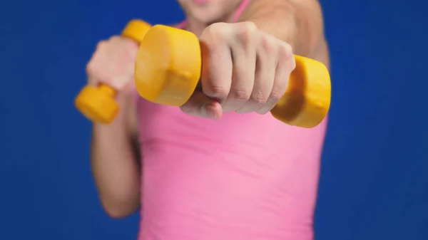 Um homem de t-shirt cor-de-rosa com um decote profundo é boxe halteres. Concentra-te nos halteres, borrão corporal. espaço de cópia — Fotografia de Stock