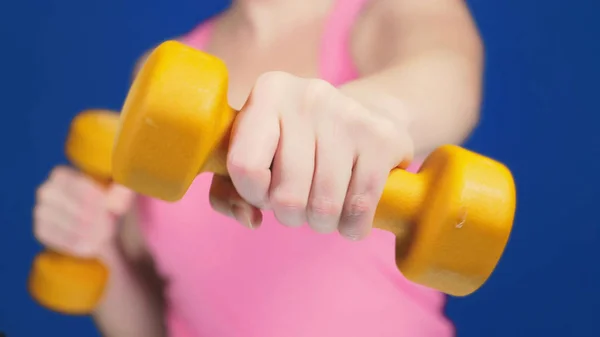 Una mujer con una camiseta rosa con un escote profundo es mancuernas de boxeo. Concéntrate en pesas, cuerpo borroso. espacio de copia — Foto de Stock