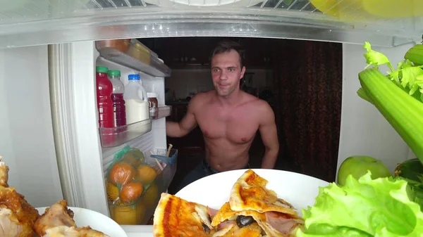 Ein junger muskulöser Mann öffnet nachts den Kühlschrank. Nachthunger. Ernährung. Völlerei — Stockfoto