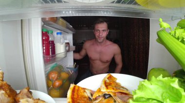 A young muscular man opens the refrigerator at night. night hunger. diet. gluttony clipart