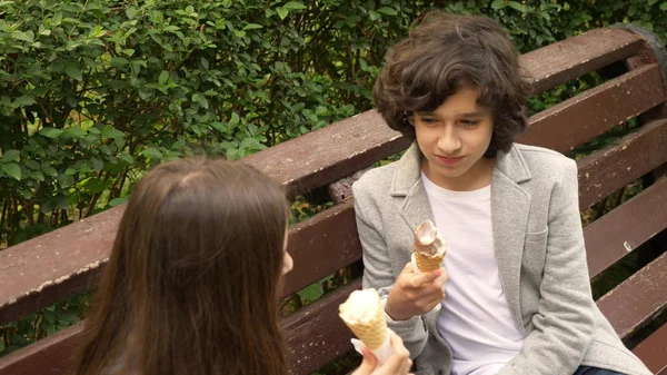 Adolescentes lindos, chico y chica comiendo helado en el parque y hablando — Foto de Stock