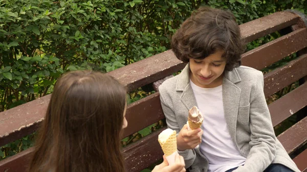 Adolescentes lindos, chico y chica comiendo helado en el parque y hablando — Foto de Stock