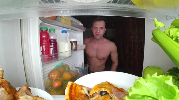 Un joven musculoso abre el refrigerador por la noche. hambre nocturna. dieta. gula —  Fotos de Stock