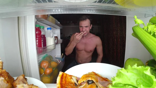 Un joven musculoso abre el refrigerador por la noche. hambre nocturna. dieta. gula — Foto de Stock