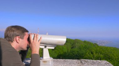 Erkek gezgin bir dağın tepesinde bir teleskop aracılığıyla arıyor.