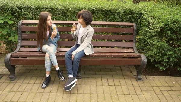 Adolescentes lindos, chico y chica comiendo helado en el parque y hablando — Foto de Stock