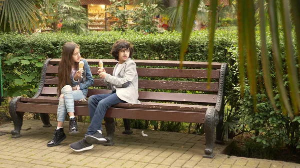 Adolescentes lindos, chico y chica comiendo helado en el parque y hablando — Foto de Stock