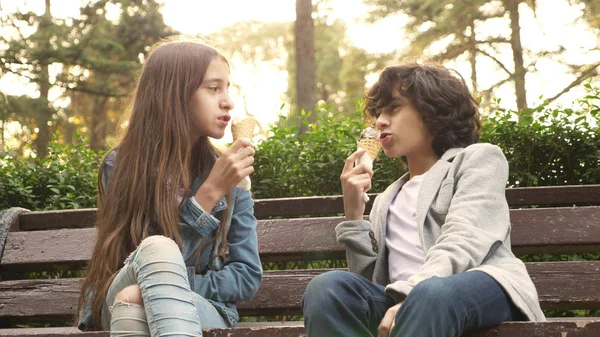 Roztomilý dospívající děti, chlapec a dívka jíst zmrzlinu v parku a mluví — Stock fotografie