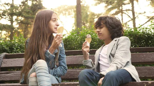 Милые подростки, мальчик и девочка едят мороженое в парке и говорят — стоковое фото
