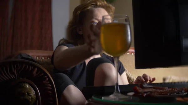 Mujer con computadora, bebiendo cerveza en casa en la oscuridad . — Foto de Stock