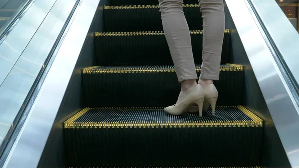 As pernas de uma mulher de calças bege, em sapatos bege em pé em uma escada rolante em movimento — Fotografia de Stock