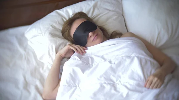 Mujer joven en una máscara para dormir, durmiendo en la cama sobre una almohada durante el día — Foto de Stock