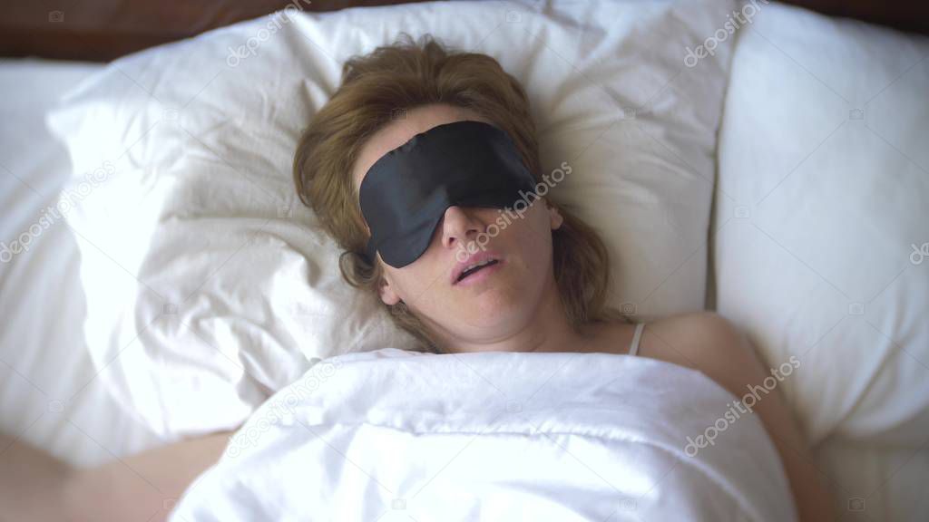 Young woman in a mask for sleeping, sleeping in bed on a pillow in the daytime