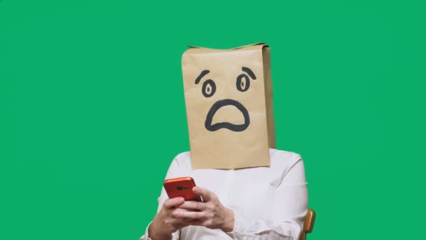 Concepto de emociones, gestos. un hombre con bolsas de papel en la cabeza, con un emoticono pintado, miedo. hablando por un teléfono celular — Vídeo de stock