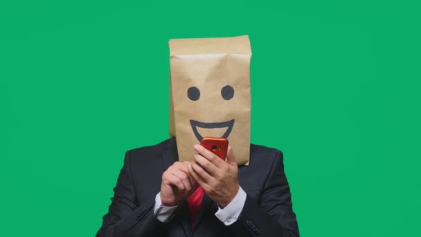 Concepto de emociones, gestos. un hombre con bolsas de papel en la cabeza, con un emoticono pintado, sonrisa, alegría. hablando por un teléfono celular — Vídeos de Stock