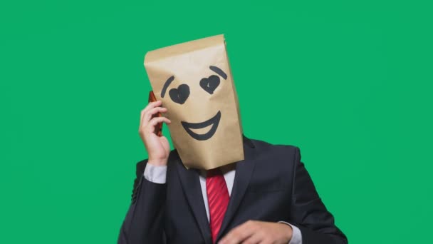 Pojmu emoce, gesta. muž s papírové sáčky na hlavě, s malovanými emotikonu, úsměv, radost, láska. mluví o mobilní telefon — Stock video
