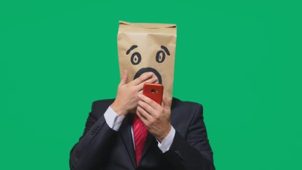 Koncepcja emocje, gesty. człowiek z torby papierowe na głowie, z malowane emotikon, strach. rozmowy na telefon komórkowy — Wideo stockowe