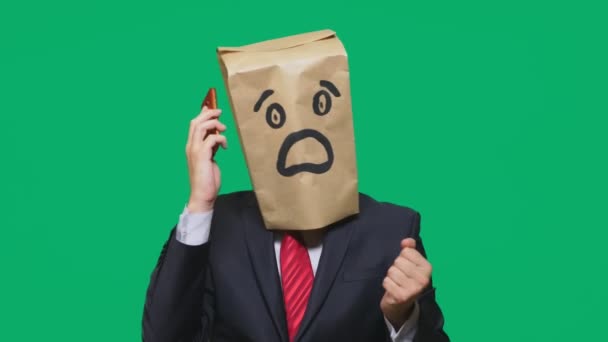 Konzept der Emotionen, Gesten. ein Mann mit Papiertüten auf dem Kopf, mit einem aufgemalten Emoticon, Angst. Telefonieren auf dem Handy — Stockvideo