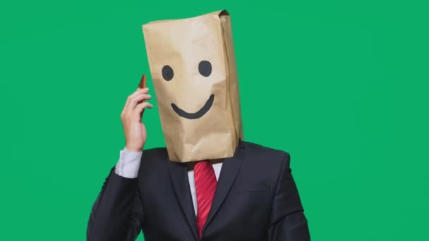 Concepto de emociones, gestos. un hombre con bolsas de papel en la cabeza, con un emoticono pintado, sonrisa, alegría. hablando por un teléfono celular — Vídeos de Stock